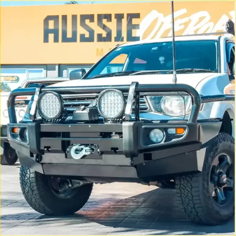 Black metal rockarmor rock pack bullbar with two circular led lights and winch mount on white mitsubishi triton 2009-2015