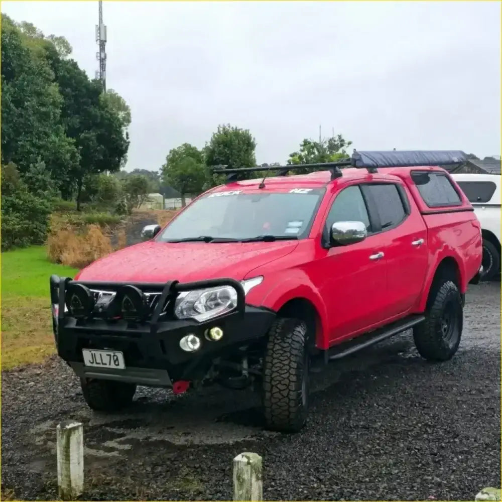 Red mitsubishi triton pickup with black roof rack and front bumper featuring gt hoop bullbar and rock sliders